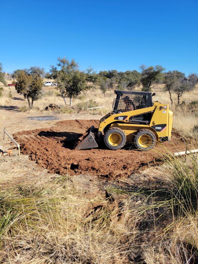 Using a skid-steer tractor to clear off vegetation and to establish a rough grade.